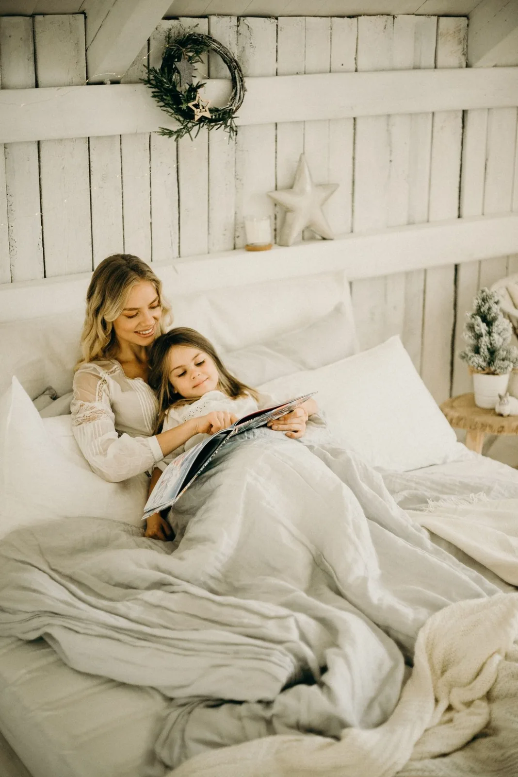 Madre e hija leyendo juntas en una cama con mantas y luz natural